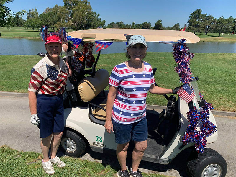 Two golfers wearing patriotic clothing beside a golf cart decorated with American flags and red, white, and blue garland.
