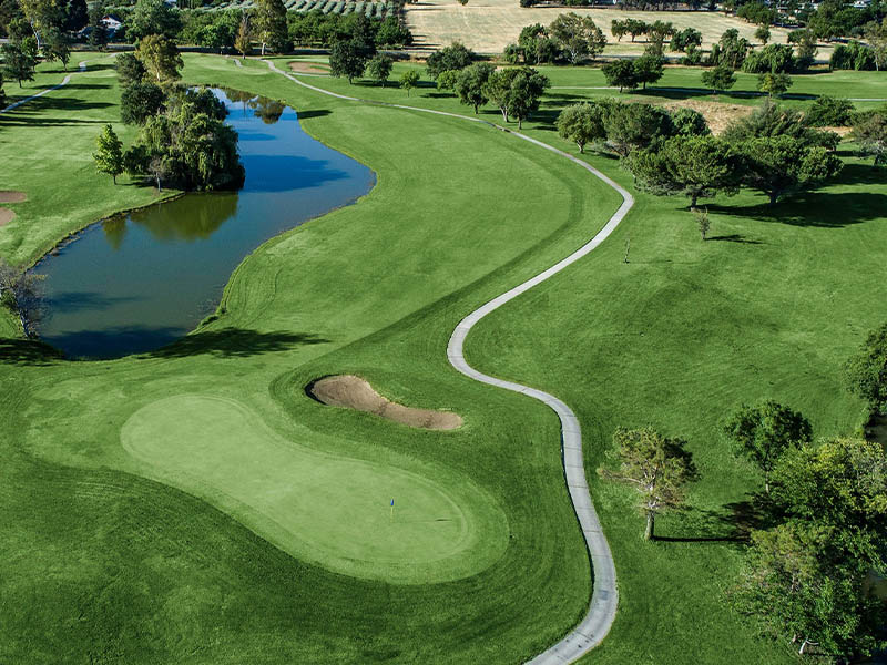 Aerial view of a Micke Grove Golf Links green, sand bunker, winding cart path, fairway, and water hazard.